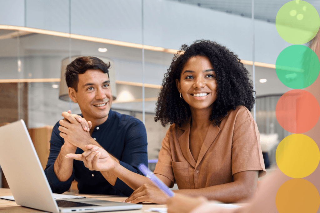 Two professionals smiling and engaged in a meeting at a modern office conference table, with colorful branded circle graphics overlaid on the right side of the image.