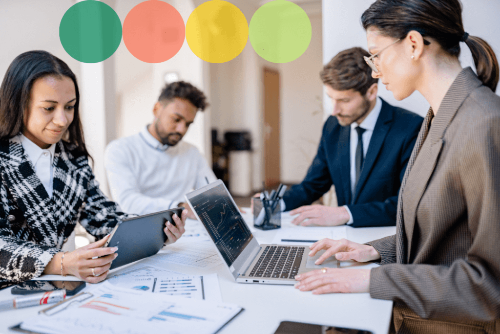 A diverse team of four professionals collaborating around a table with laptops and printed data reports.