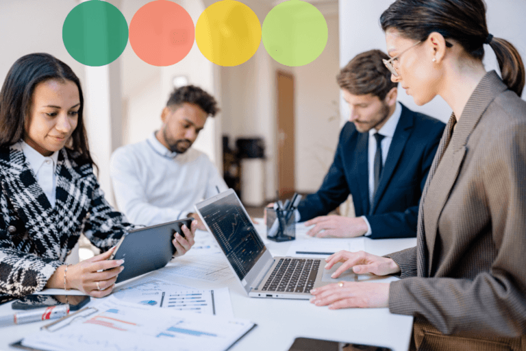 A diverse team of four professionals collaborating around a table with laptops and printed data reports.