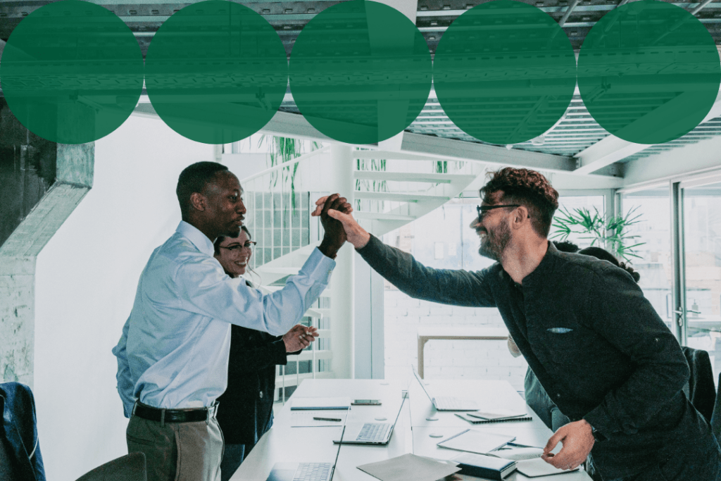 Two colleagues celebrate with a high five across a conference table in a bright, modern office.