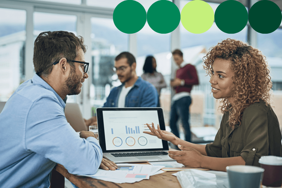 Two professionals discussing data analytics displayed on a laptop screen in a busy open office environment, with dark green, light green, and yellow-green branded circle graphics overlaid along the top of the image.