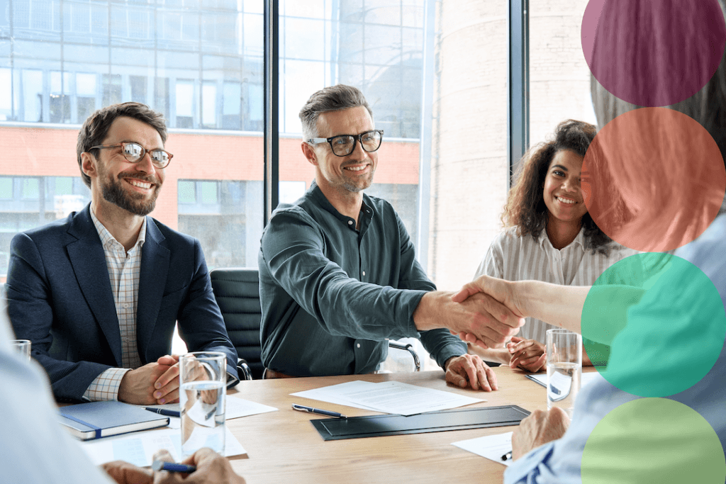 A group of smiling business professionals shaking hands across a conference table during a meeting.