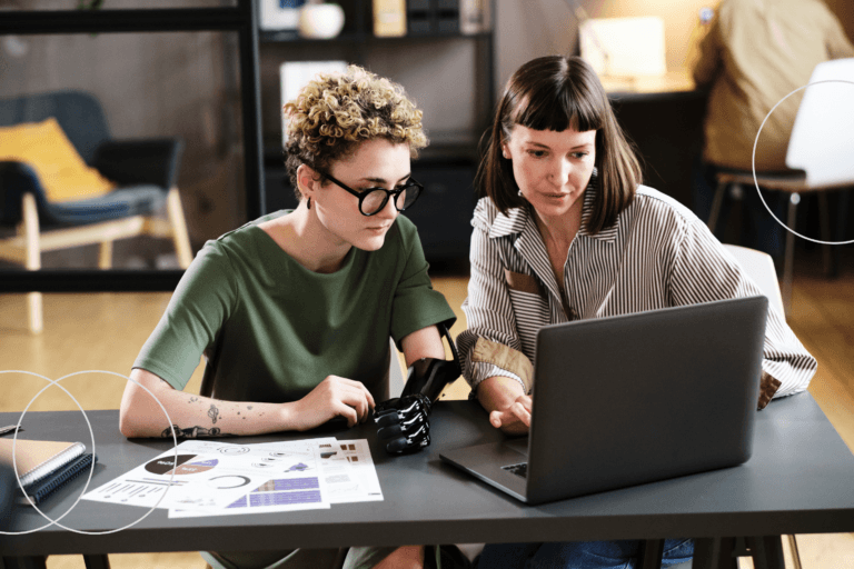 Two diverse professionals reviewing supplier data on a laptop in a modern office setting.