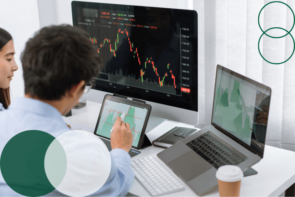 Two professionals analyzing data charts across multiple screens and a tablet in a modern office setting, with dark green and white branded circle graphics overlaid in the corners of the image.