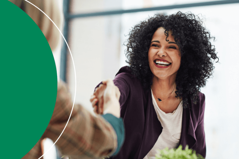 A woman smiling and shaking hands during a professional meeting, with a green branded circle graphic overlaid on the left side of the image.