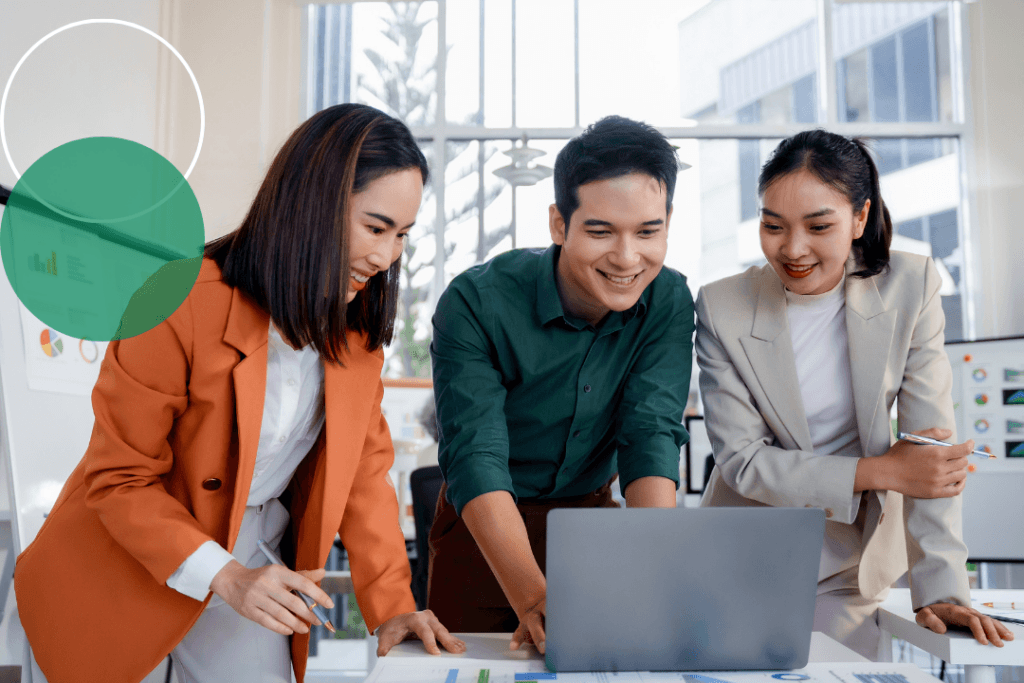 Three business professionals collaborating enthusiastically around a laptop in a bright office environment, with green and white branded circle graphics overlaid in the top left corner.