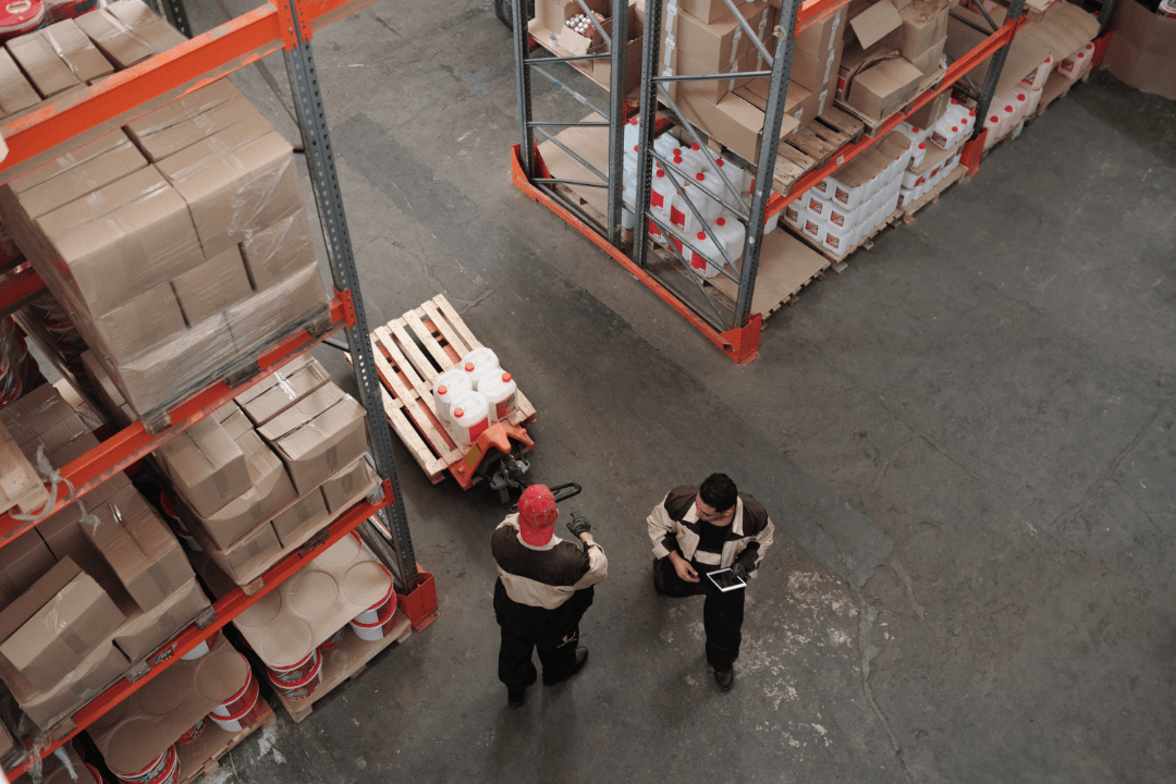 Aerial view of two warehouse workers managing inventory among shelved pallets and boxes.