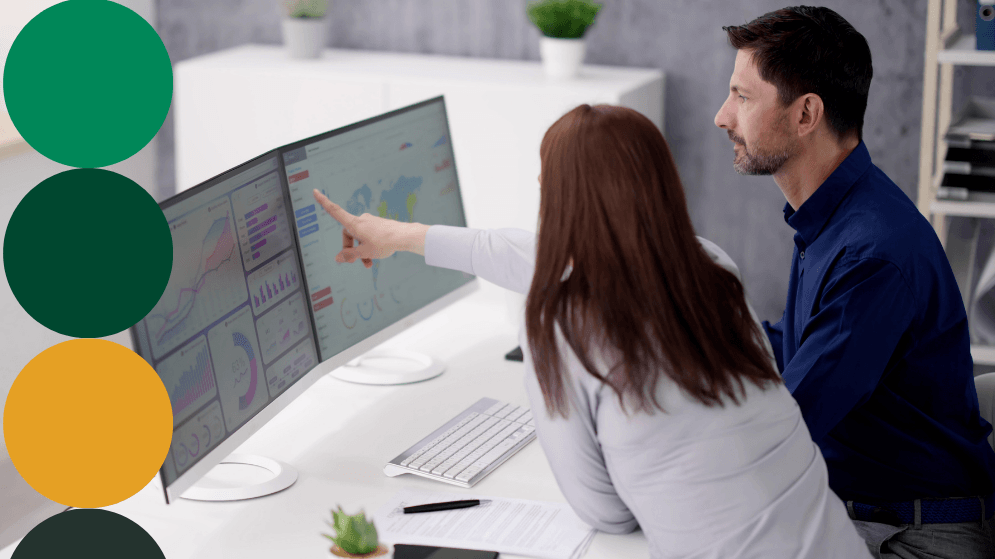 Two procurement professionals reviewing supplier data dashboards on dual monitors, with one pointing at a spend analytics chart