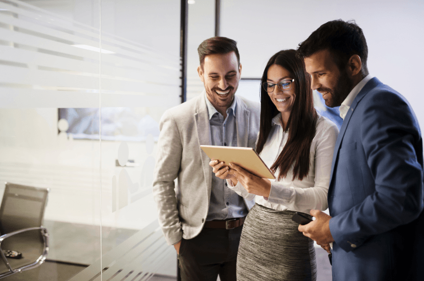 Three business professionals reviewing data on a tablet in an office setting