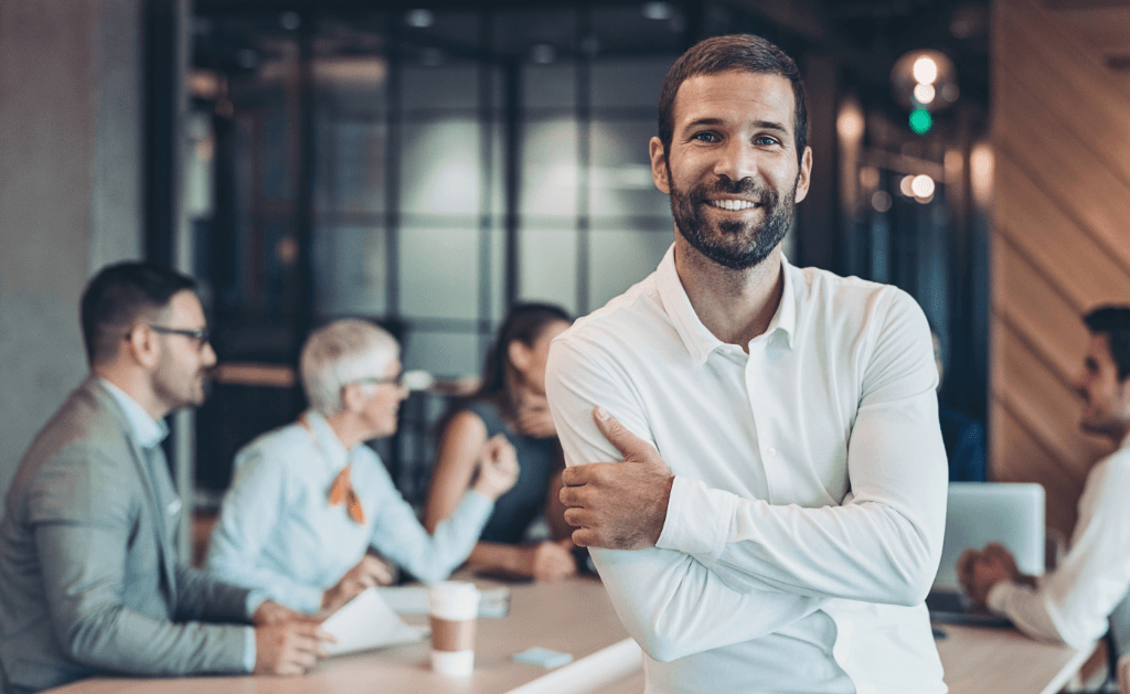 Procurement professional standing confidently with arms crossed, team collaborating in the background