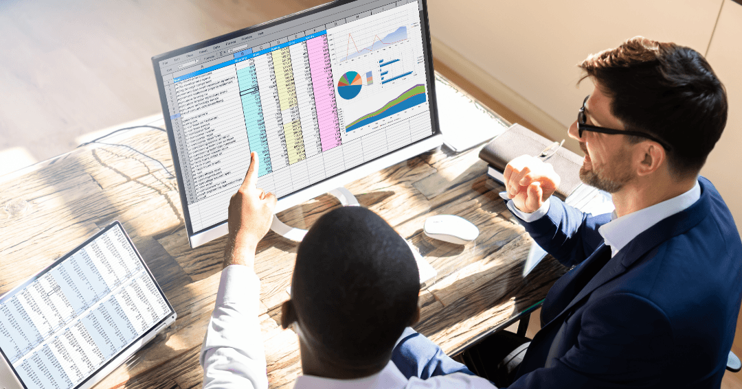 Two colleagues reviewing spreadsheet data and charts on a desktop monitor