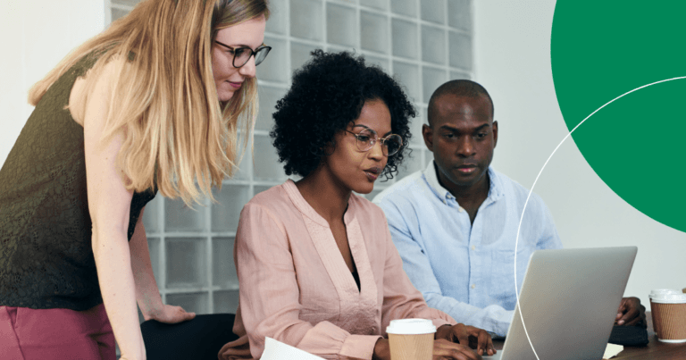 Three professionals reviewing data together on a laptop in an office setting.