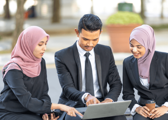 Three business colleagues in professional attire reviewing a laptop together outdoors.