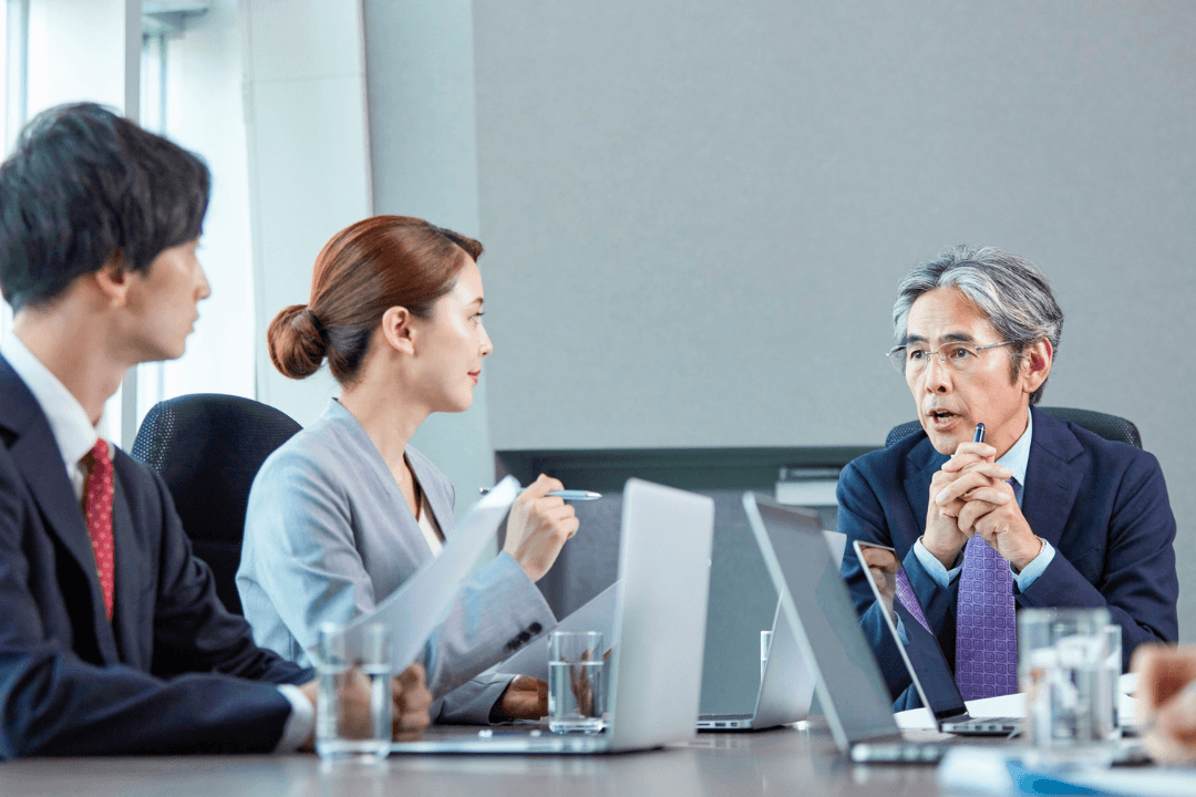 Business colleagues seated at a conference table with open laptops, discussing during a meeting.